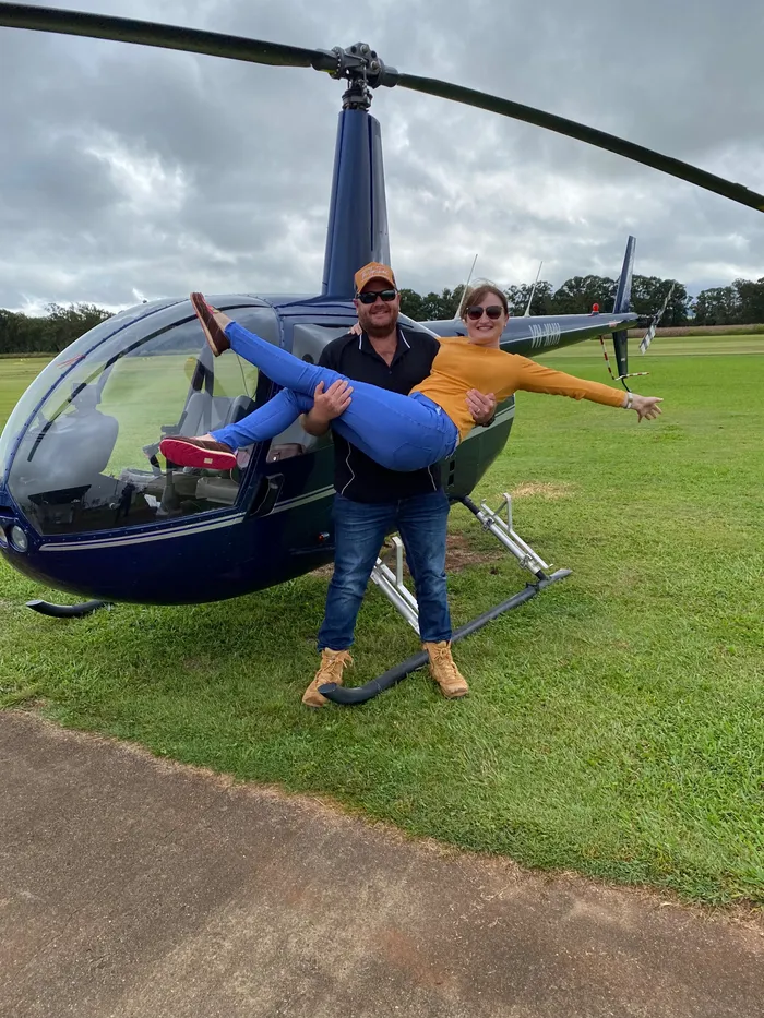 Trevor lifting a laughing passenger in front of a helicopter on the Tablelands.