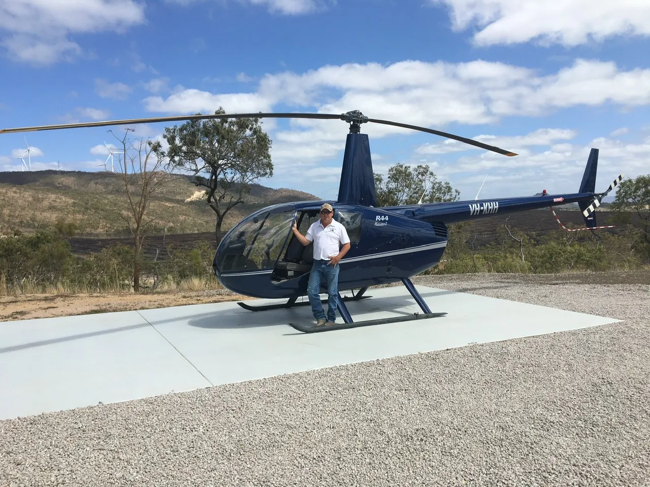 Trevor standing beside his helicopter on a remote helipad in the Tablelands, hills in the background.