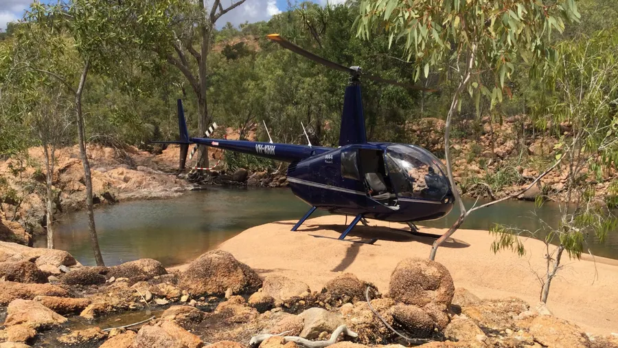 A helicopter landed on a sandbar beside a creek, surrounded by bushland.
