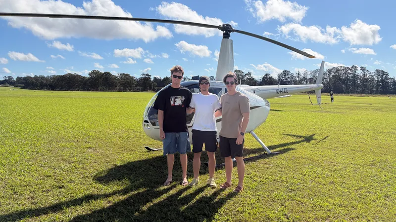 Three passengers smiling in front of the helicopter on the grass at Atherton Aerodrome before a scenic flight.