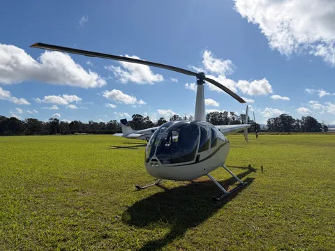 A helicopter parked on the grass at Atherton Aerodrome on a sunny day.