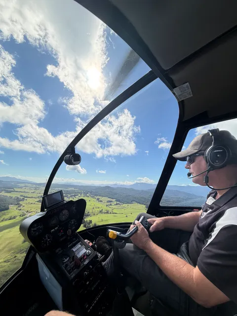 Trevor flying over green farmland and distant mountains.
