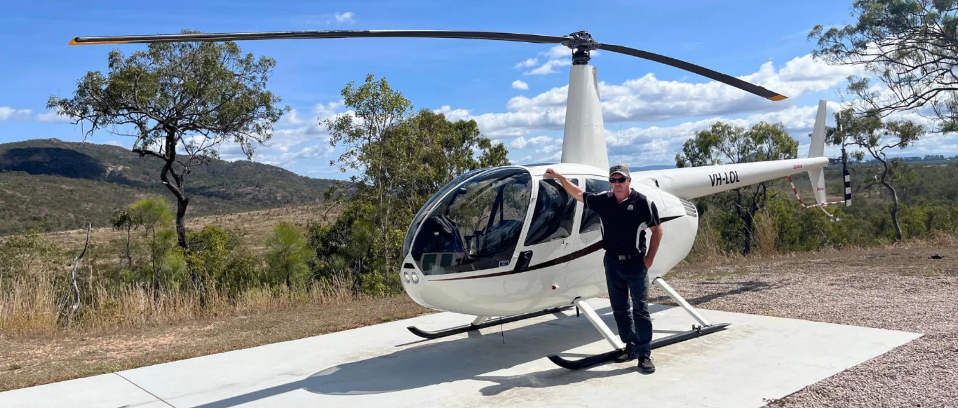 Trevor standing beside the helicopter on a remote hilltop landing pad in the Tablelands.